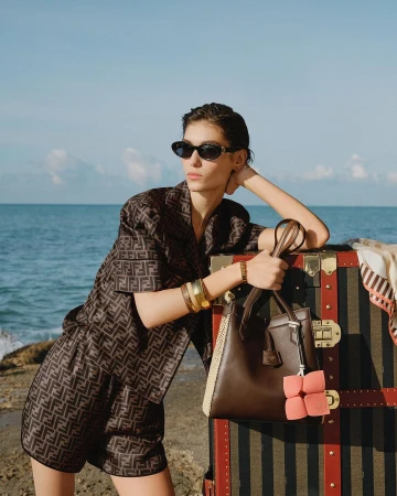 Model in monogram matching set and sunglasses leaning against a large vintage trunk by the ocean by photographer Ellen Fedors