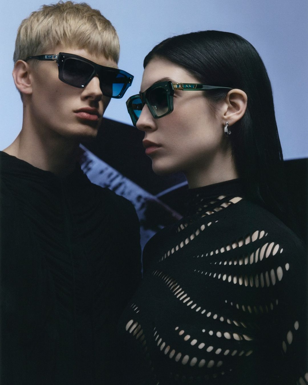 A stylish fashion editorial featuring a pair of models showcasing eyewear. The focus is on the design and aesthetics of the sunglasses.