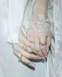Close-up of two hands holding each other wearing detailed rings and lace sleeves, photographed by Ellen Nykvist