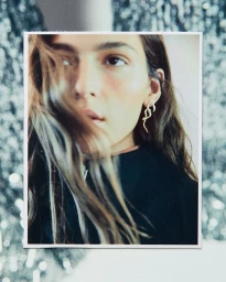 Close-up portrait of a woman wearing a serpentine gold earring against a blurred glittering background.