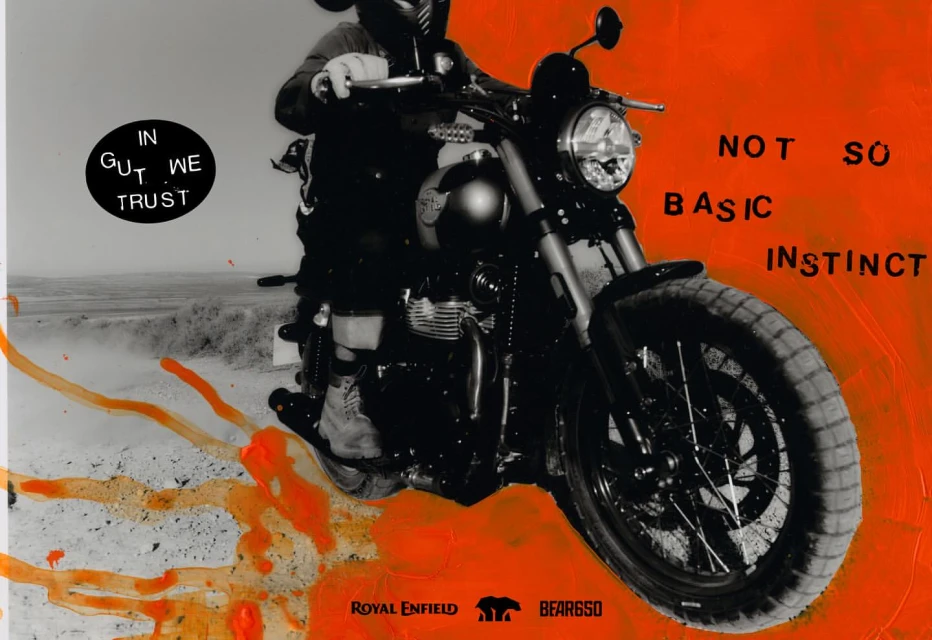 Motorcycle rider on a black scrambler-style motorbike in an outdoor desert environment, presented in a stylized, artistic advertising image.
