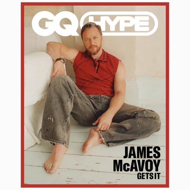 James McAvoy on GQ Hype cover: The adult male celebrity sits cross-legged on the floor wearing a red shirt and grey jeans in a studio setting.