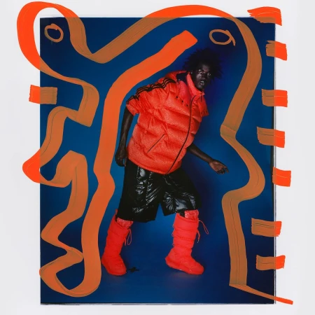 Fashion shot of person in orange puffer vest, black shorts, and orange boots against blue backdrop with orange abstract shapes.