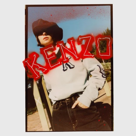 Fashion shot of a woman in a beret, sweater, and jeans, posing outdoors with the word KENZO spray-painted in red across the image.