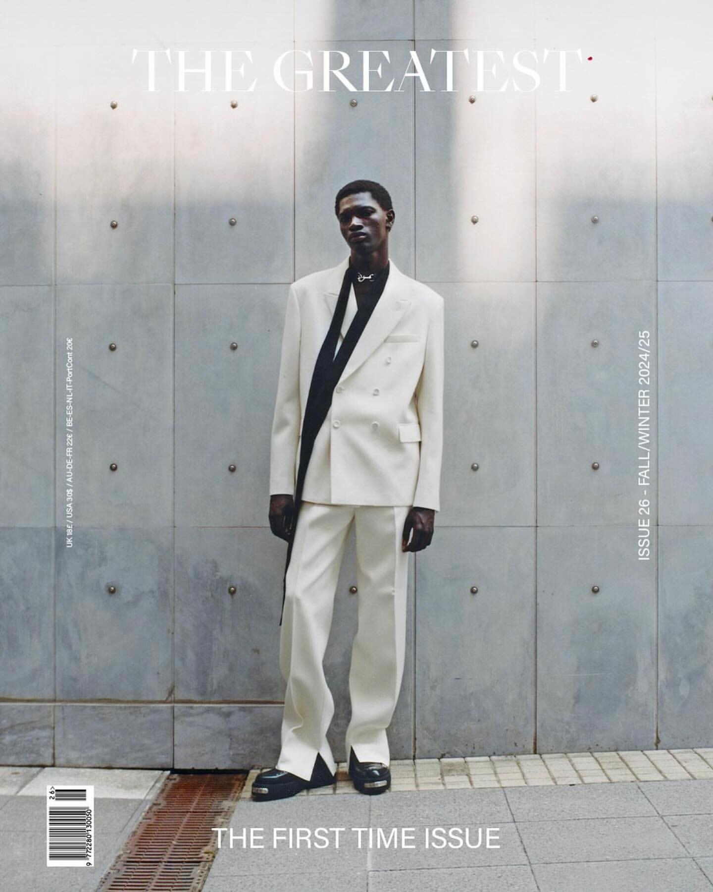 Magazine cover featuring a male model in a light suit against a concrete wall, with "The Greatest" and "The First Time Issue" text.