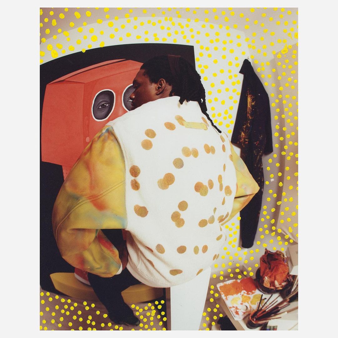Person from behind wearing a white polka-dot top, standing in front of an orange art piece and white wall dotted with yellow.