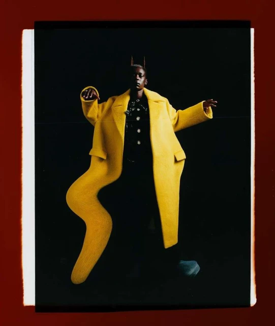 A woman in a vibrant yellow coat poses against a dark backdrop, showcasing a blend of fashion and abstract visual elements.