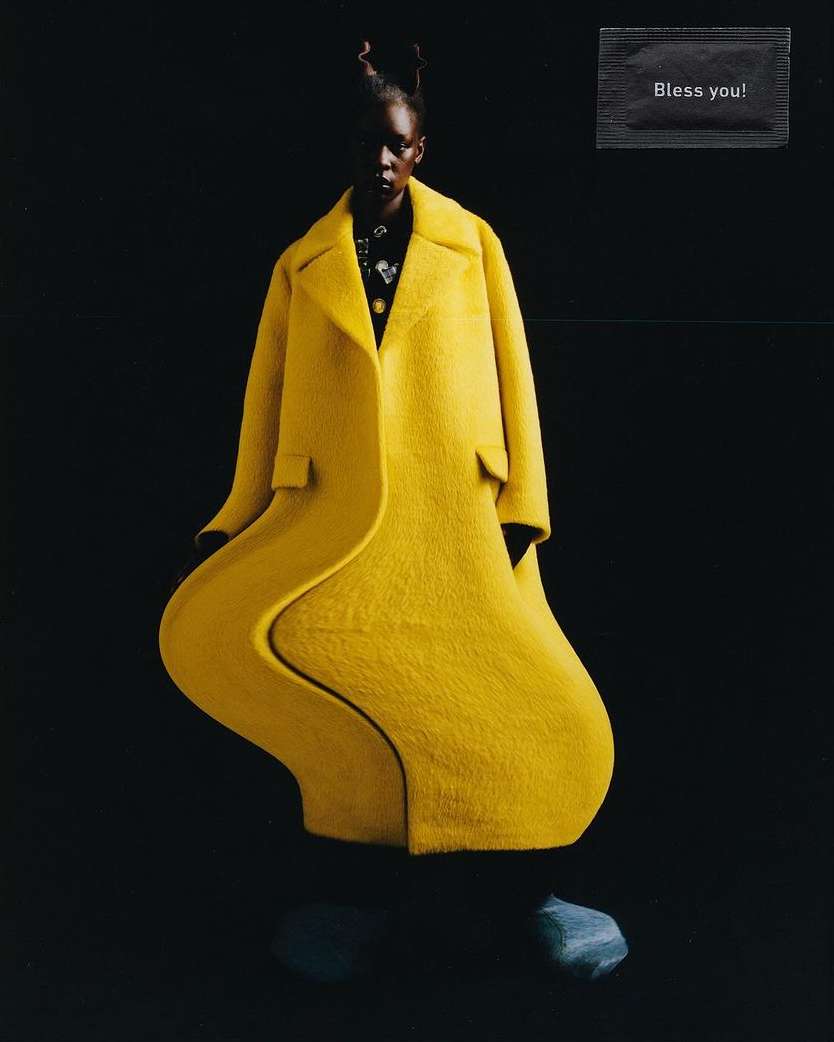 Fashion shot of a dark-skinned woman in a bright yellow coat against a black background with a surreal, wavy effect applied to the coat.