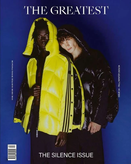 Fashion magazine cover featuring two models in hooded puffer jackets, one yellow and one black, against a blue background.