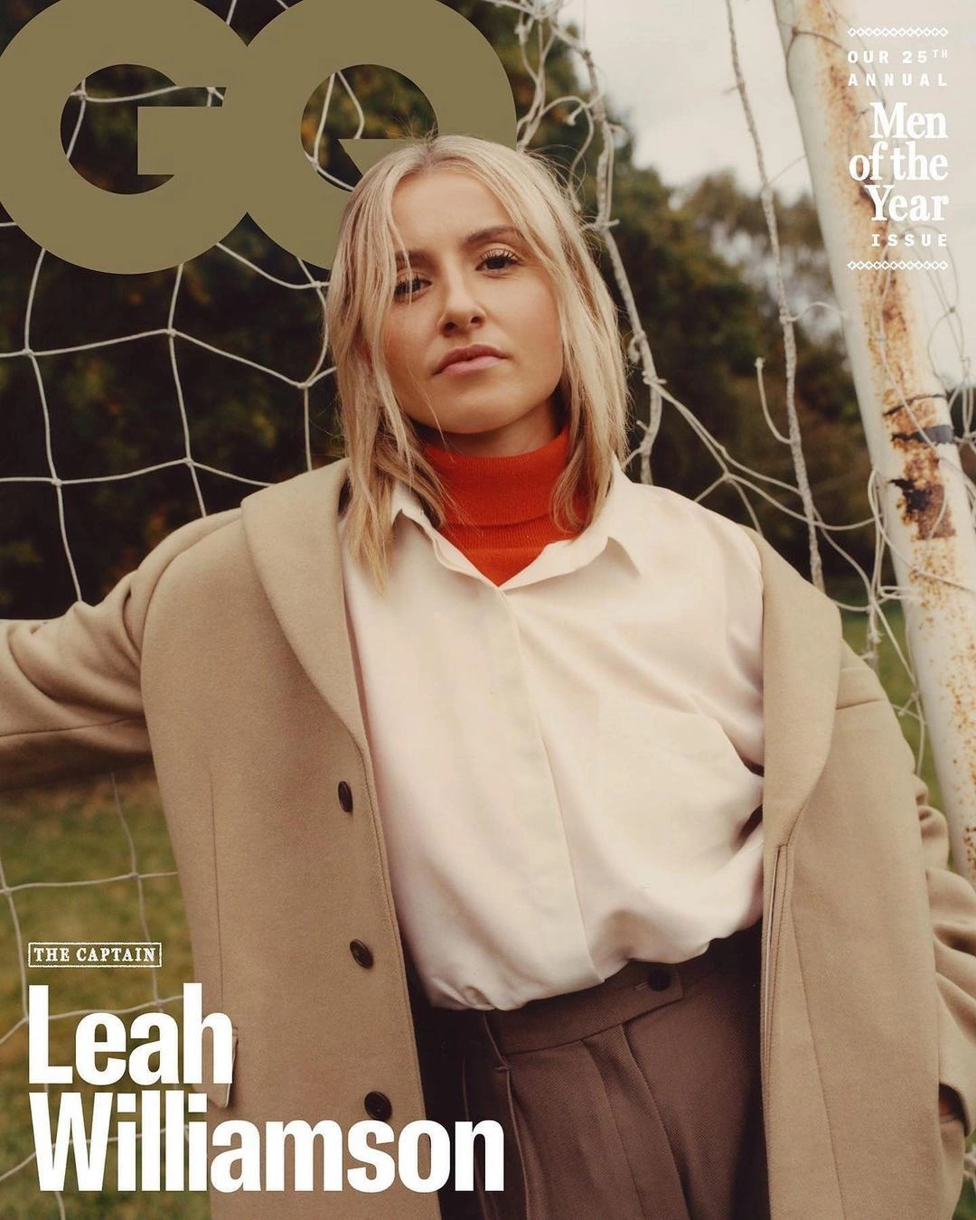 Leah Williamson standing in front of a soccer net wearing an overcoat, white shirt, and orange turtleneck.