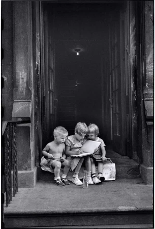 Three young children sitting together on a building doorstep reading a book in Milan by Elliott Erwitt.