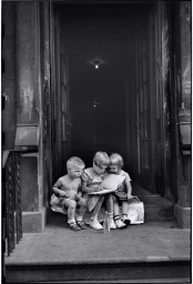Three young children sitting together on a building doorstep reading a book in Milan by Elliott Erwitt.