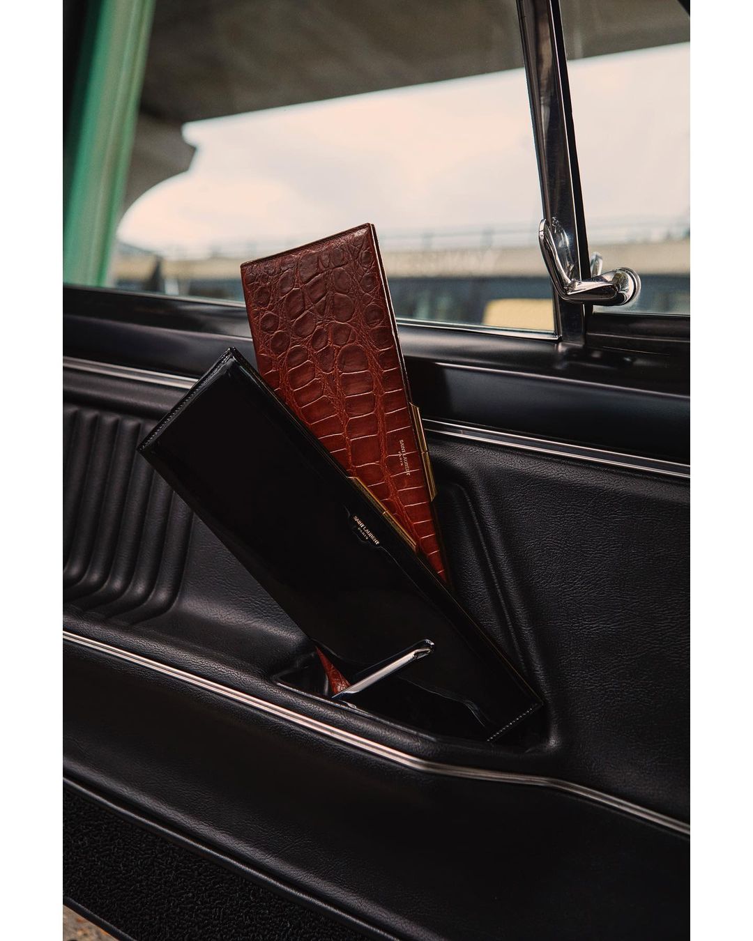 A brown crocodile skin wallet and a black wallet are visible in the inside pocket of a black car door panel.