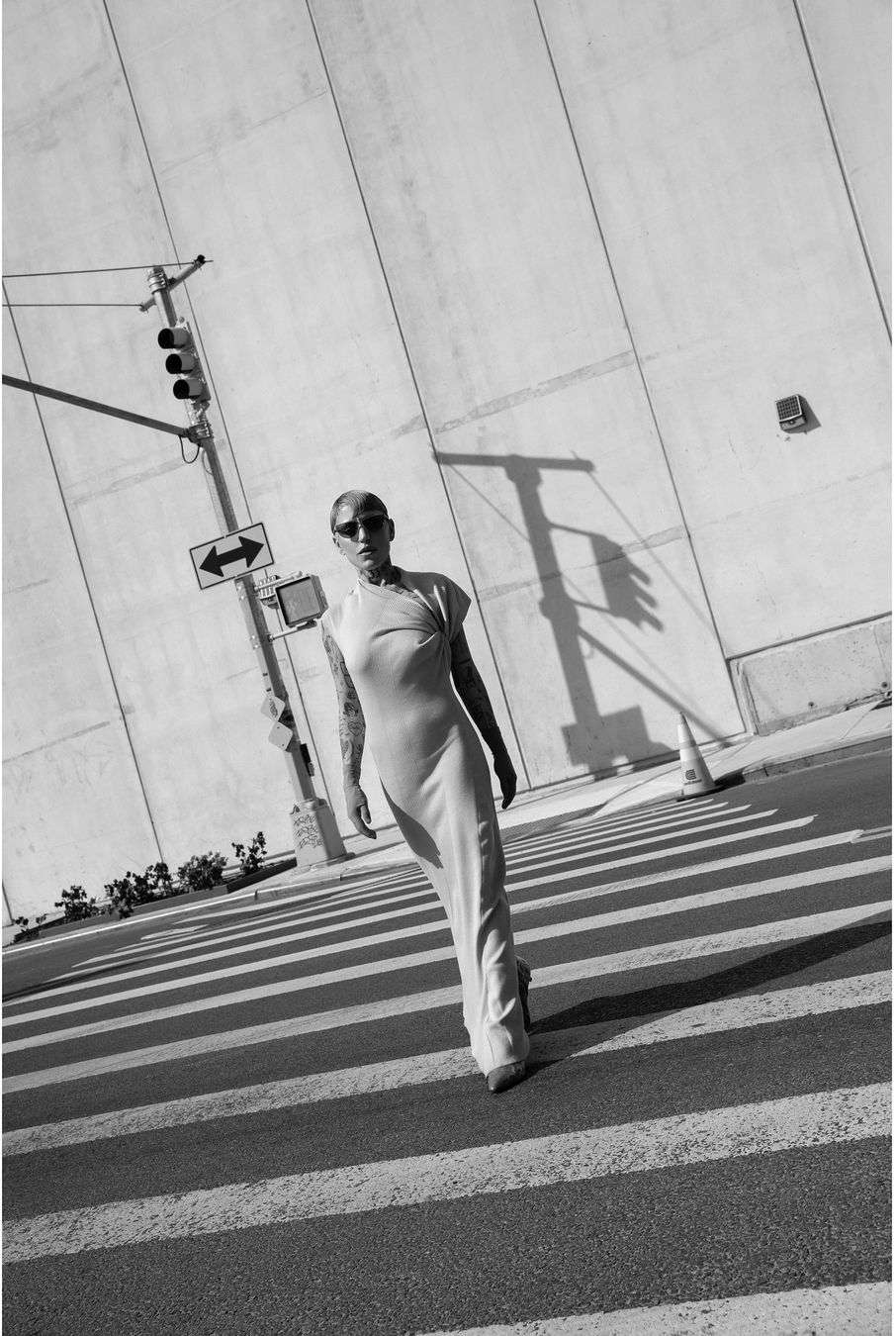 A person in a dress walks across a crosswalk in an urban setting, with a traffic light and a large building in the background.