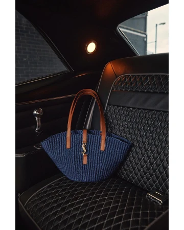Saint Laurent bag on a quilted leather car seat with brown leather handles. The handbag is mostly navy and black with gold logo.