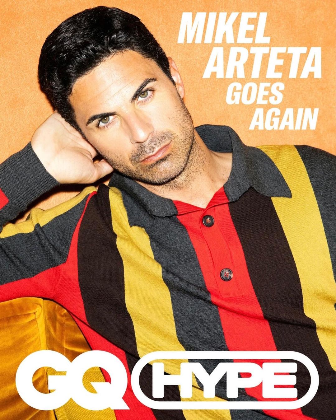 Adult male poses in vertical studio shot wearing striped red, yellow, and gray polo shirt with GQ Hype magazine logo.