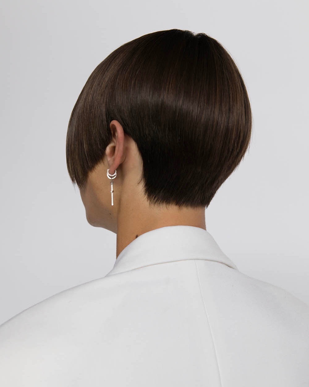 Brunette woman wearing a white jacket in a studio setting with diffused lighting showcasing short layered hair and silver earrings.