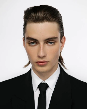 Portrait of a man with slicked-back hair wearing a black suit and tie against a white background by Elliott Morgan