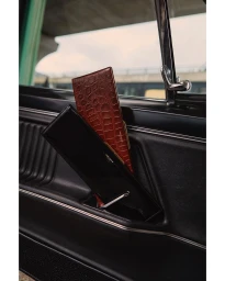Two slim leather wallets held in the side door pocket of a classic black car interior photographed by Elliott Morgan.