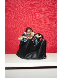 Black leather handbag with ornate religious figurine nestled inside, set against a vibrant red patterned background.