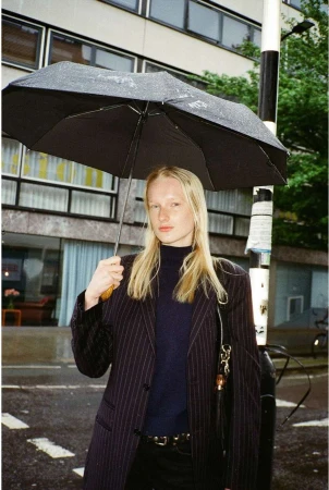 Blonde woman holding a black umbrella wearing a pinstripe blazer outdoors in London by Elliott Morgan