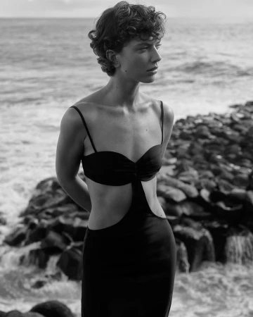 Monochrome portrait of a woman with curly hair wearing a cutout dress by the rocky coast in London by Ellyse Anderson.
