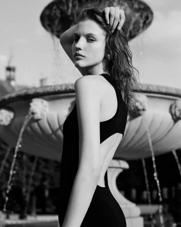 Monochrome portrait of a woman in a black backless dress posing near an outdoor stone fountain in London.