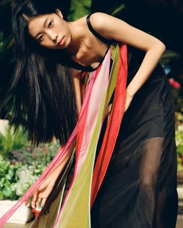 East Asian woman with long dark hair wearing a black dress with colourful pink and green ribbons outdoors in London.