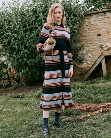 Red-haired woman in a striped midi shirt dress holding a duck in a grassy outdoor setting.