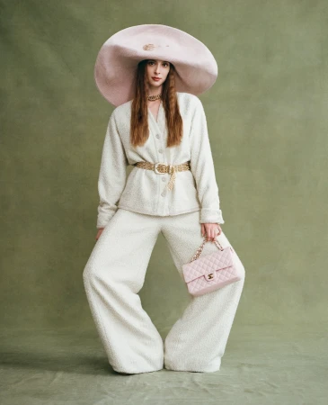 Fashionable woman poses in white suit and oversized hat holding pink purse against an olive green backdrop, style, studio fashion portrait.