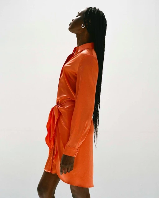 Elegant Black woman in an orange tie-front satin dress. Long braided hair and modern silver earrings complement her sophisticated look.