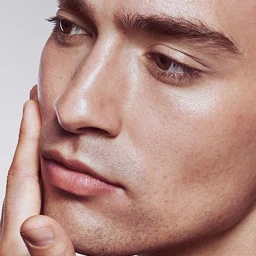 Close-up portrait of a man touching his face, showing detailed skin texture and neutral expression against a plain background