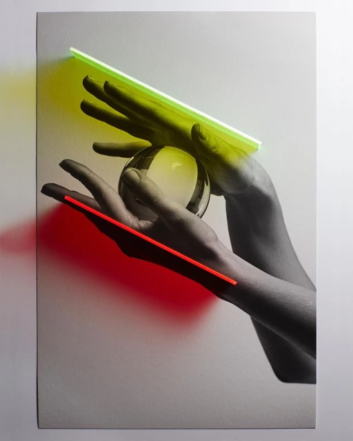 Surreal studio image of grayscale hands holding a clear sphere with red and green neon lights adding colour and sharp shadows.