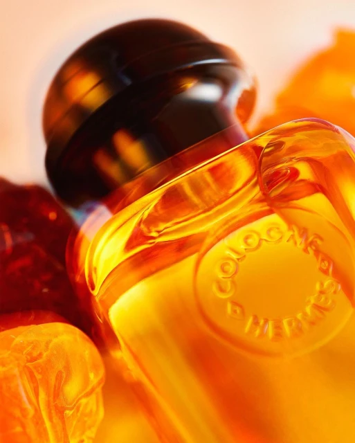 Close-up shot of a transparent glass bottle of amber liquid with a dark cap, surrounded by orange pieces, product photography.
