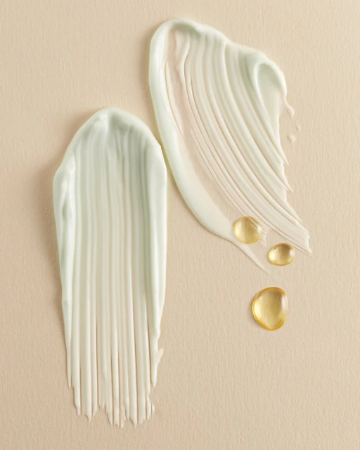 Swatches of light green cream product and drops of golden oil on a beige background, showcasing cosmetic textures for beauty advertisement.