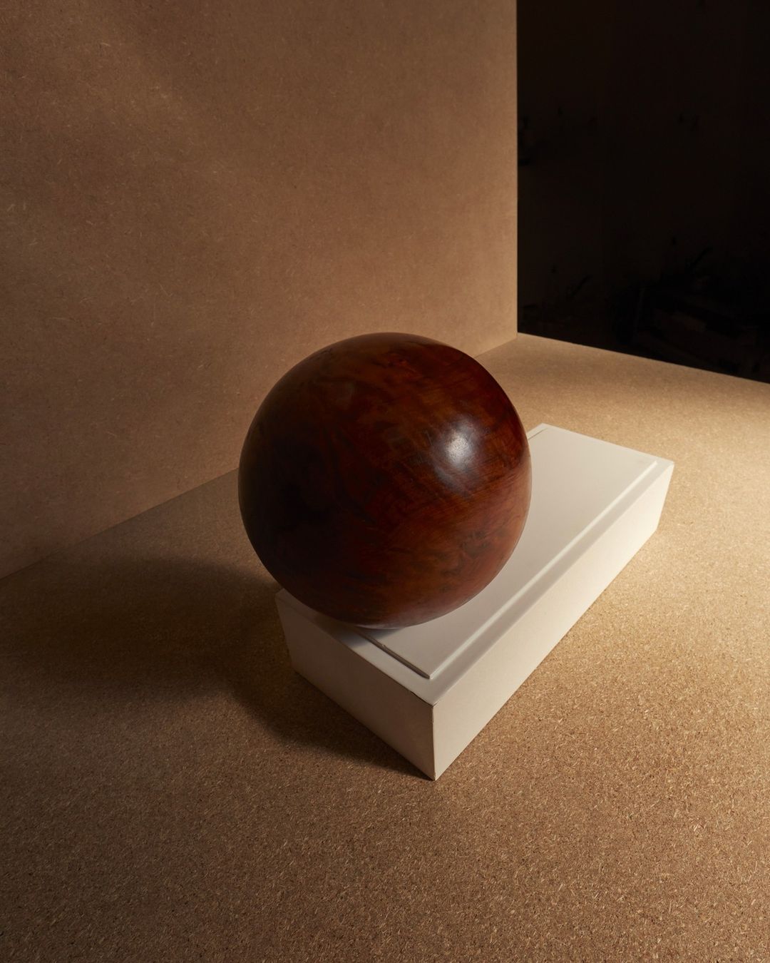 Close-up studio shot of a reddish-brown wooden sphere balanced on a white rectangular block against a neutral background.