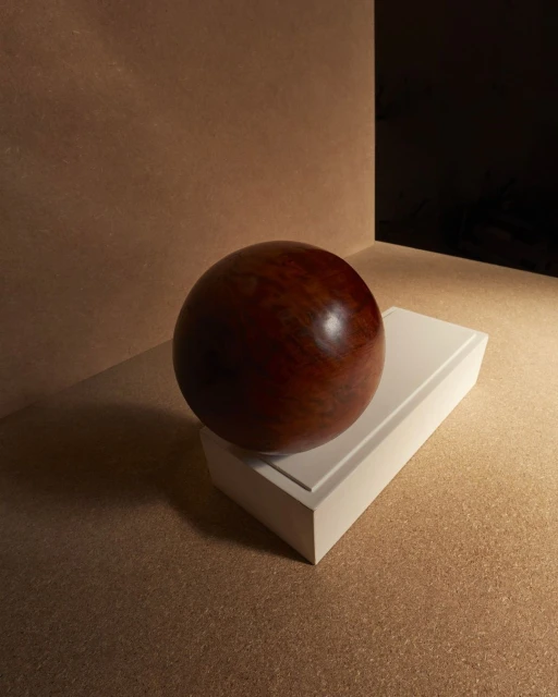 Close-up studio shot of a reddish-brown wooden sphere balanced on a white rectangular block against a neutral background.
