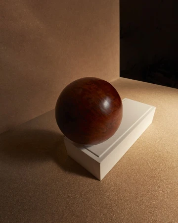 Close-up studio shot of a reddish-brown wooden sphere balanced on a white rectangular block against a neutral background.