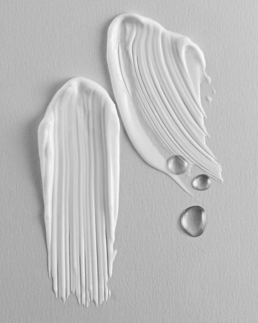 Two white cream smears and water droplets against a light gray background, showcasing texture, contrast, and product application.