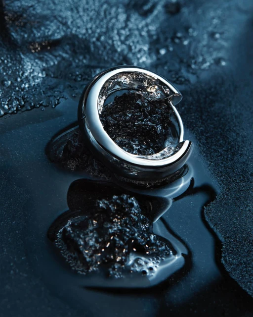 Close-up of a silver hoop earring set on a dark textured wet surface, providing a luxurious and minimalist jewelry display.