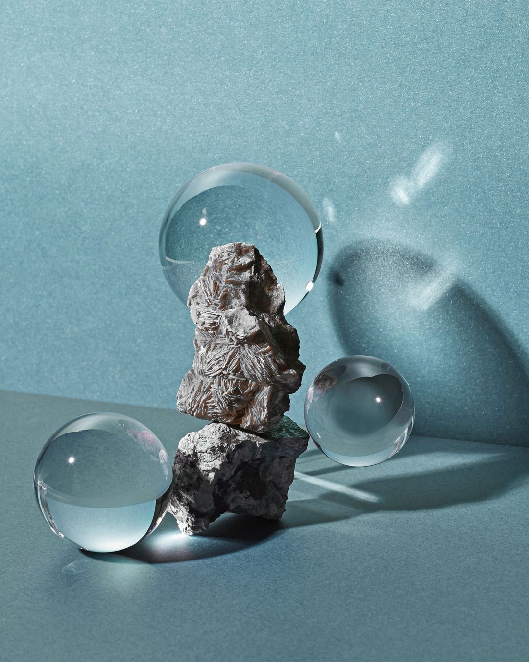 Still life featuring stacked rocks and clear crystal balls on a blue background, with cast shadows adding depth and visual interest.