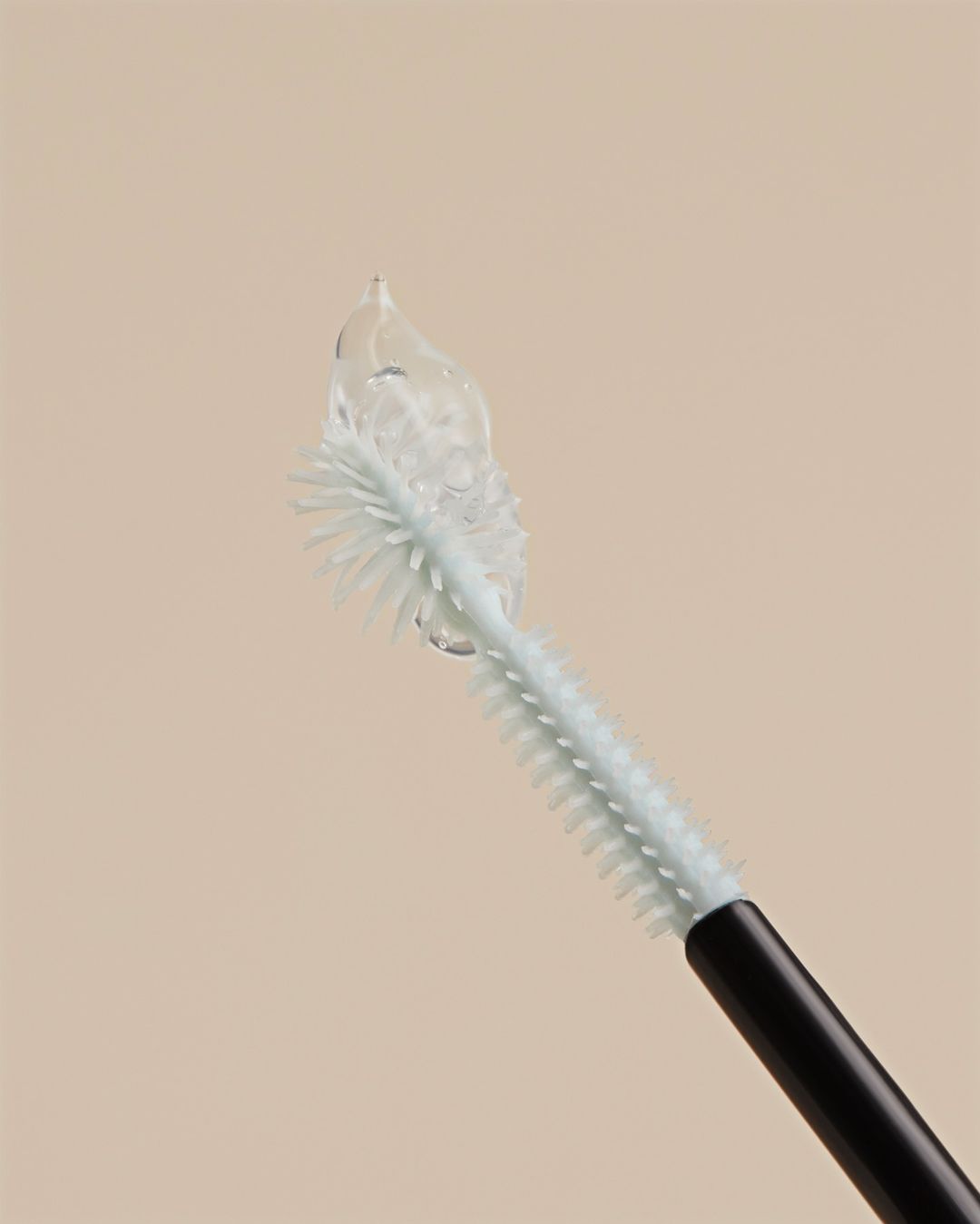 Close-up of a pale blue mascara wand with clear mascara on the bristles, against a light beige background.