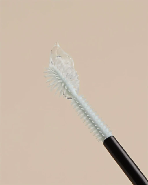 Close-up of a pale blue mascara wand with clear mascara on the bristles, against a light beige background.