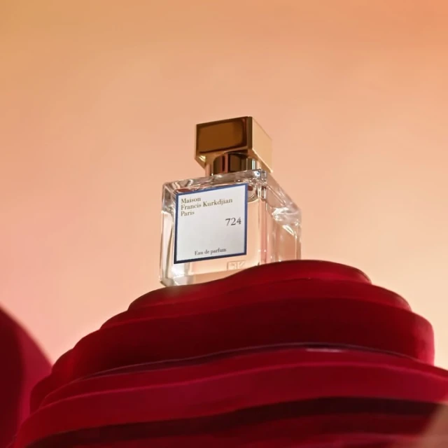 Maison Francis Kurkdjian Paris 724 perfume bottle on a red wavy surface, set against a gradient orange and white background.