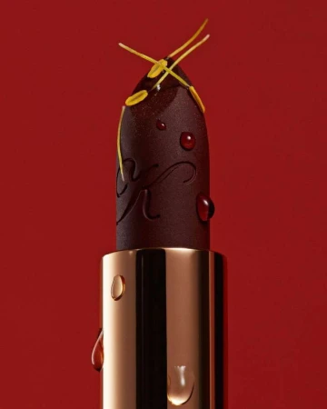 Close-up of a dark lipstick bullet with water droplets and yellow floral elements against a red background