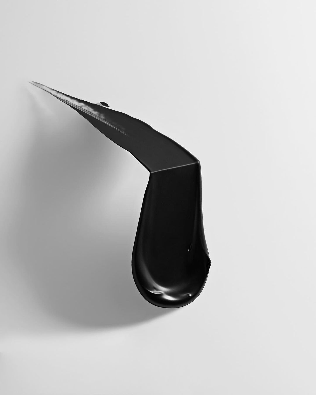 Monochrome image of a thick, glossy black cream or liquid splash against a clean white background, creating a minimalist aesthetic.