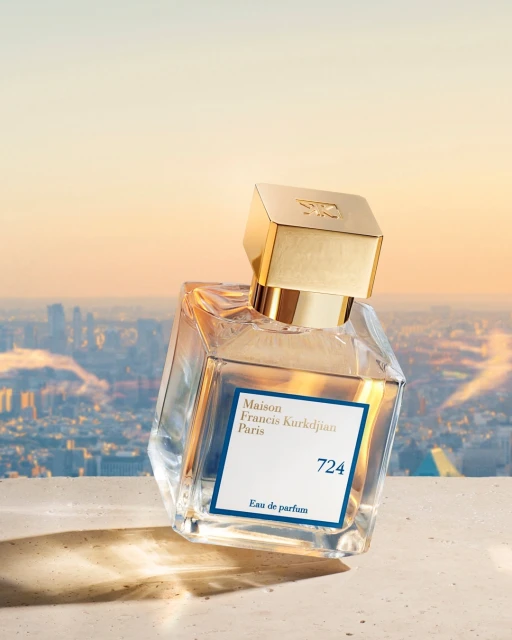 Perfume bottle of Maison Francis Kurkdjian Paris 724, against a blurred urban skyline with a golden sunset sky backdrop.