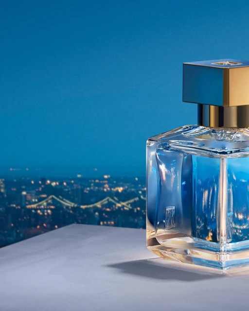 Elegant square perfume bottle with golden cap against blue backdrop featuring blurred city lights at night, creating a luxurious presentation.