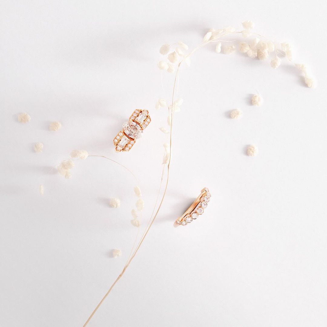 Elegant gold earrings sparkle against a pristine white backdrop. Dried floral elements add a natural, minimalist touch to the jewellery presentation.