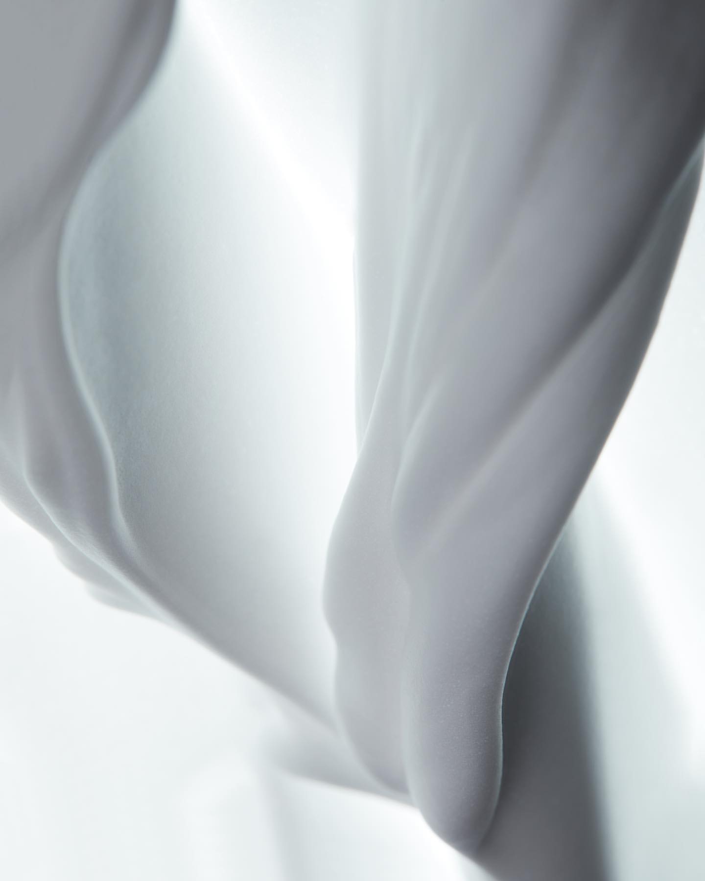 Abstract close-up of flowing white fabric with soft lighting creating depth and smooth textures, suitable for beauty and fashion themes.